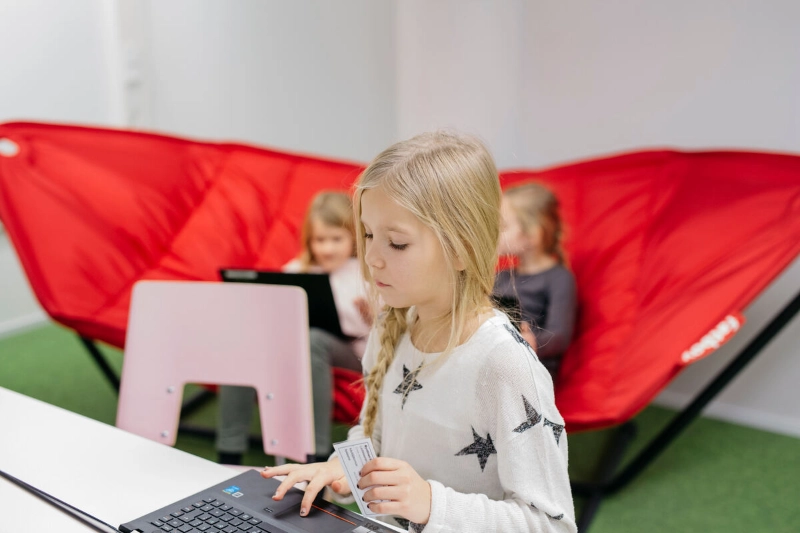 A child sits in a chair typing on a laptop. - Elina Manninen / Keksi Agency / Team Finland