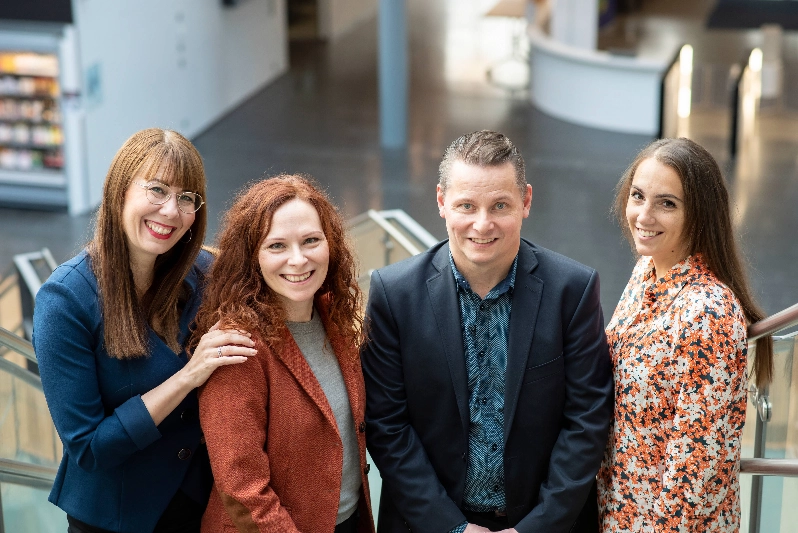 Four people look at the camera and smile happily.