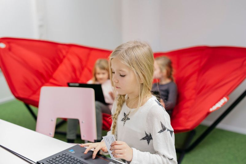 A child sits in a chair typing on a laptop. - Elina Manninen / Keksi Agency