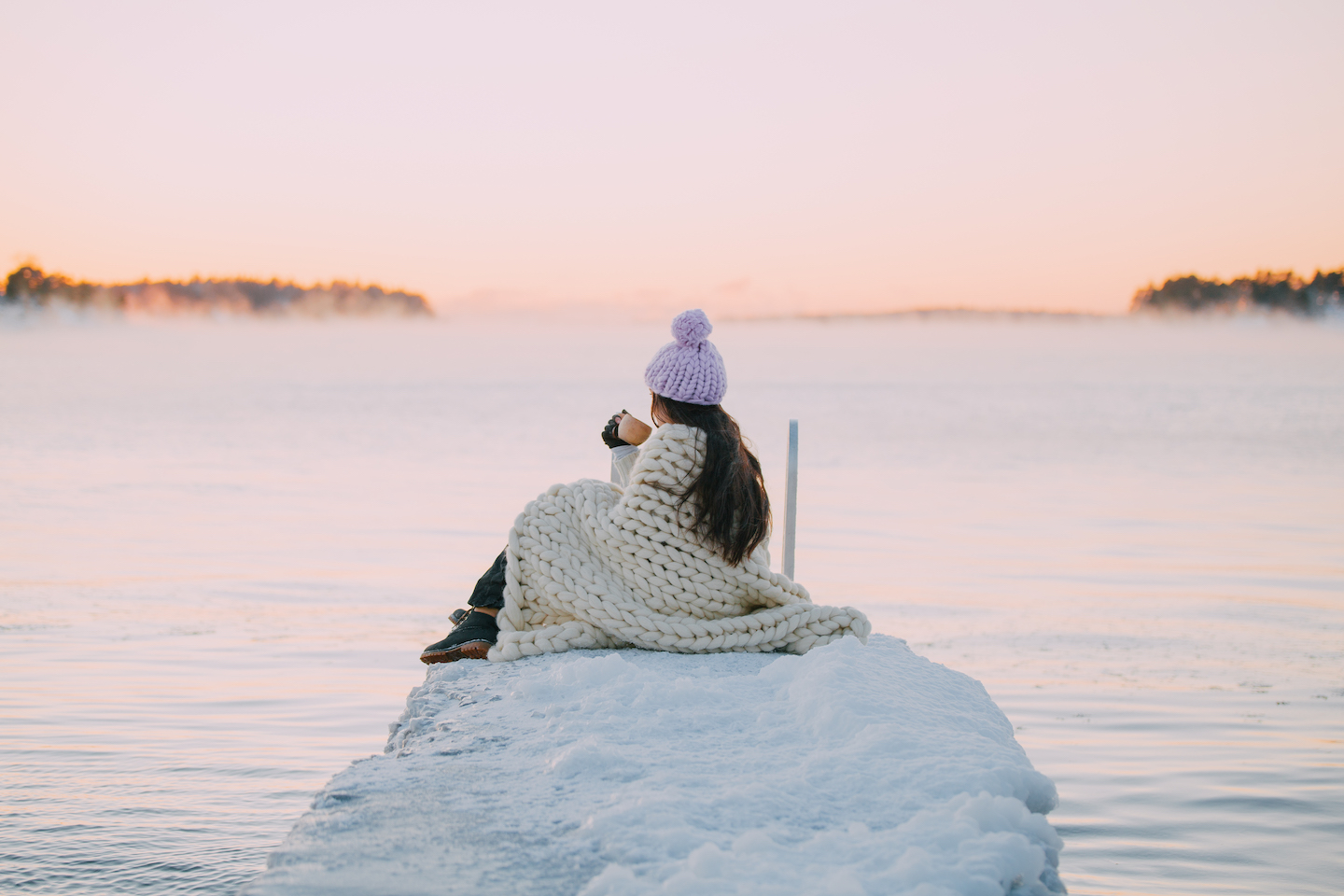 凍ったドックのそばに座り、朝の光に照らされた海の水平線を見つめる女性