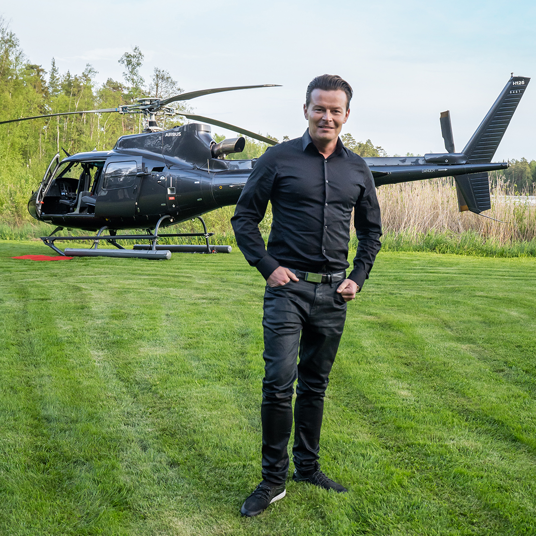 A man wearing full black outfit standing in the front of a helicopter.