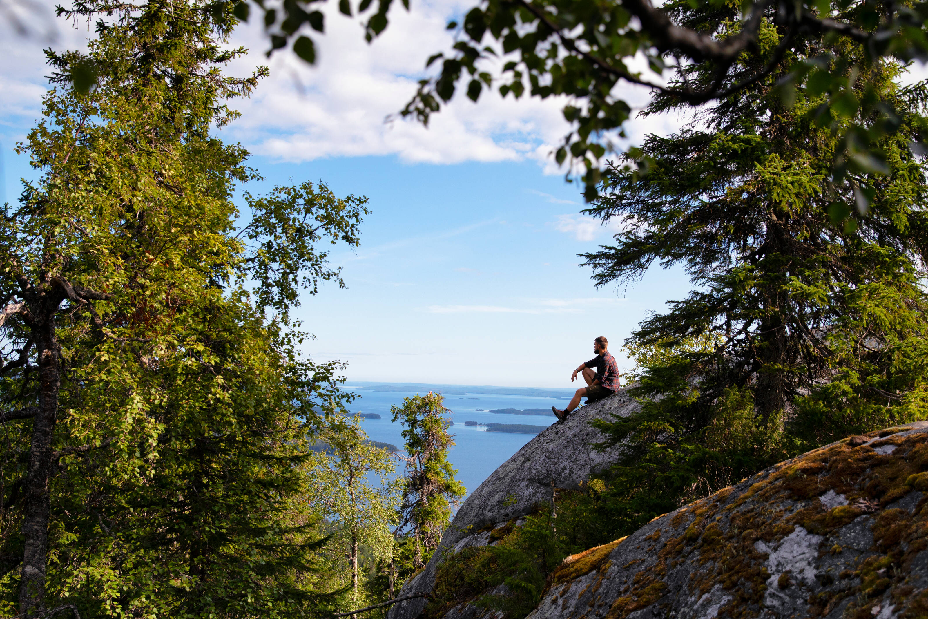 A man is sitting on a rock in front of a Lake landscape in Finland