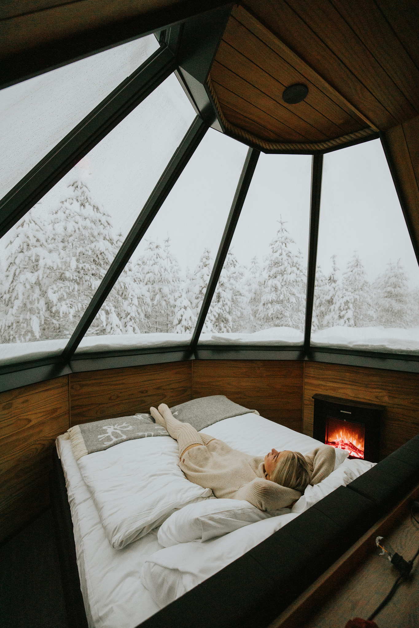 A woman laying on a bed in an aurora cabin in a snowy surroundings in Finnish Lapland.