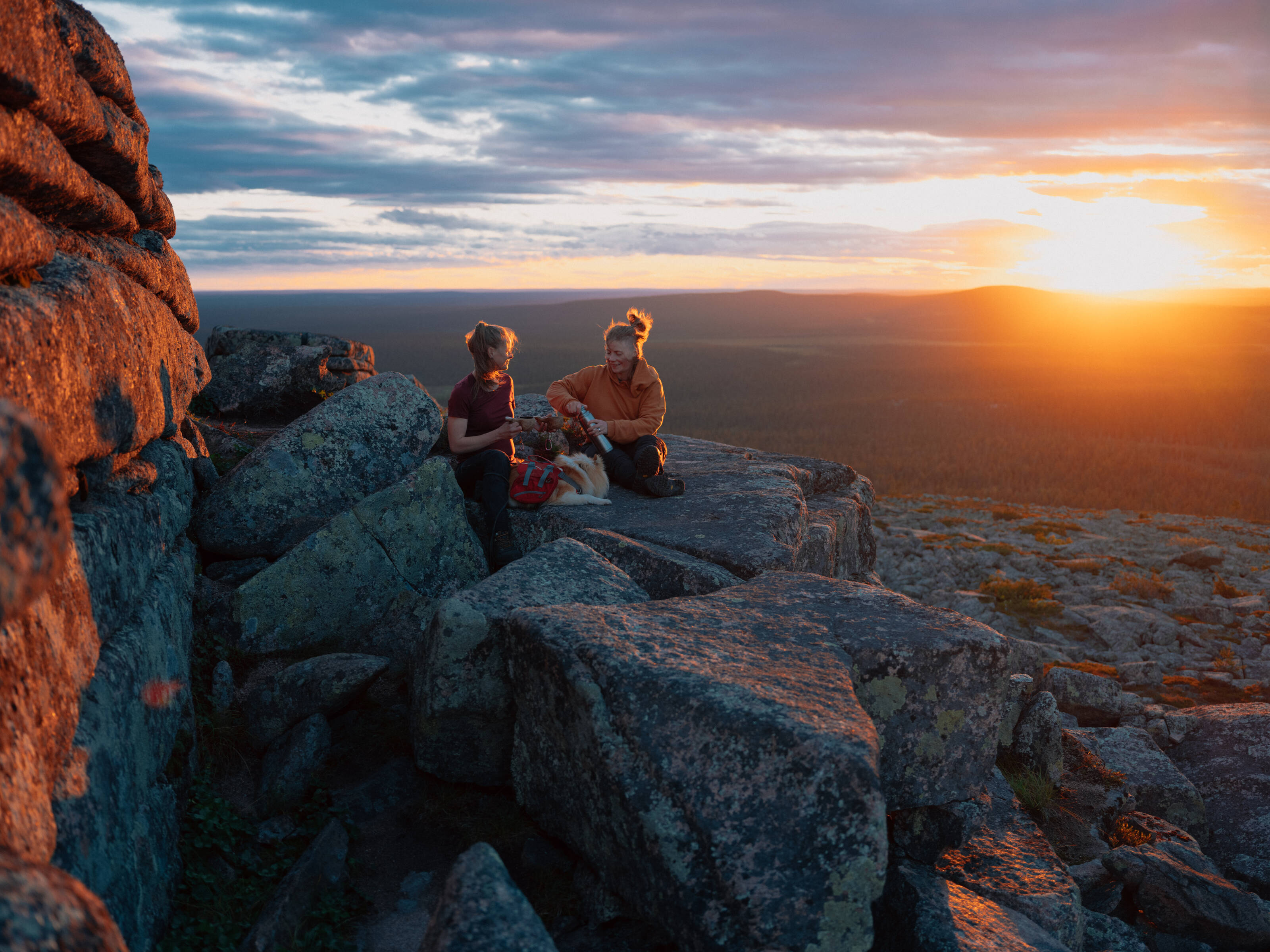 two women sitting on a fell in lapland under the midnight sun