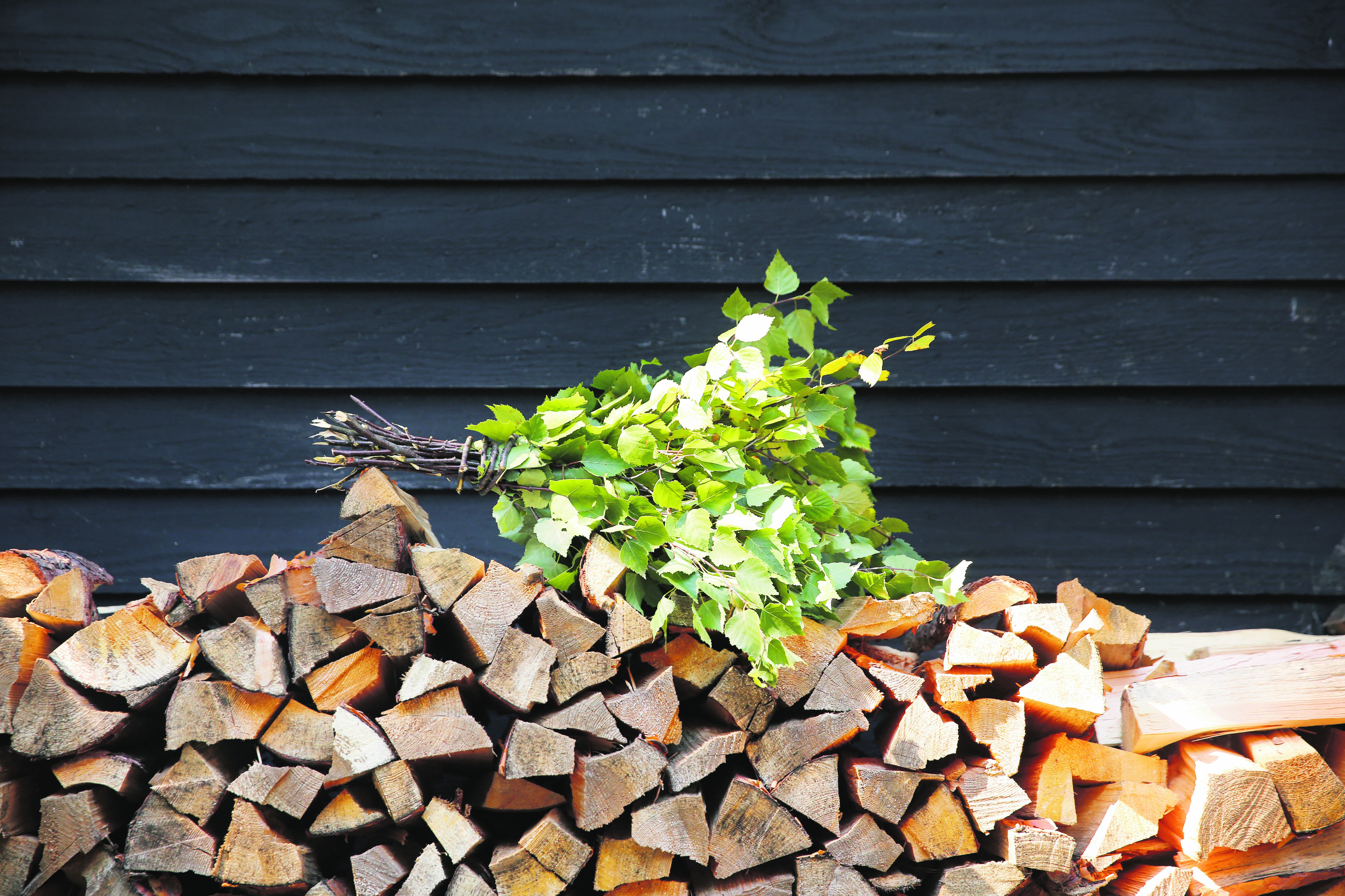 a birch whisk on firewood on the outside wall of the wooden outdoor sauna