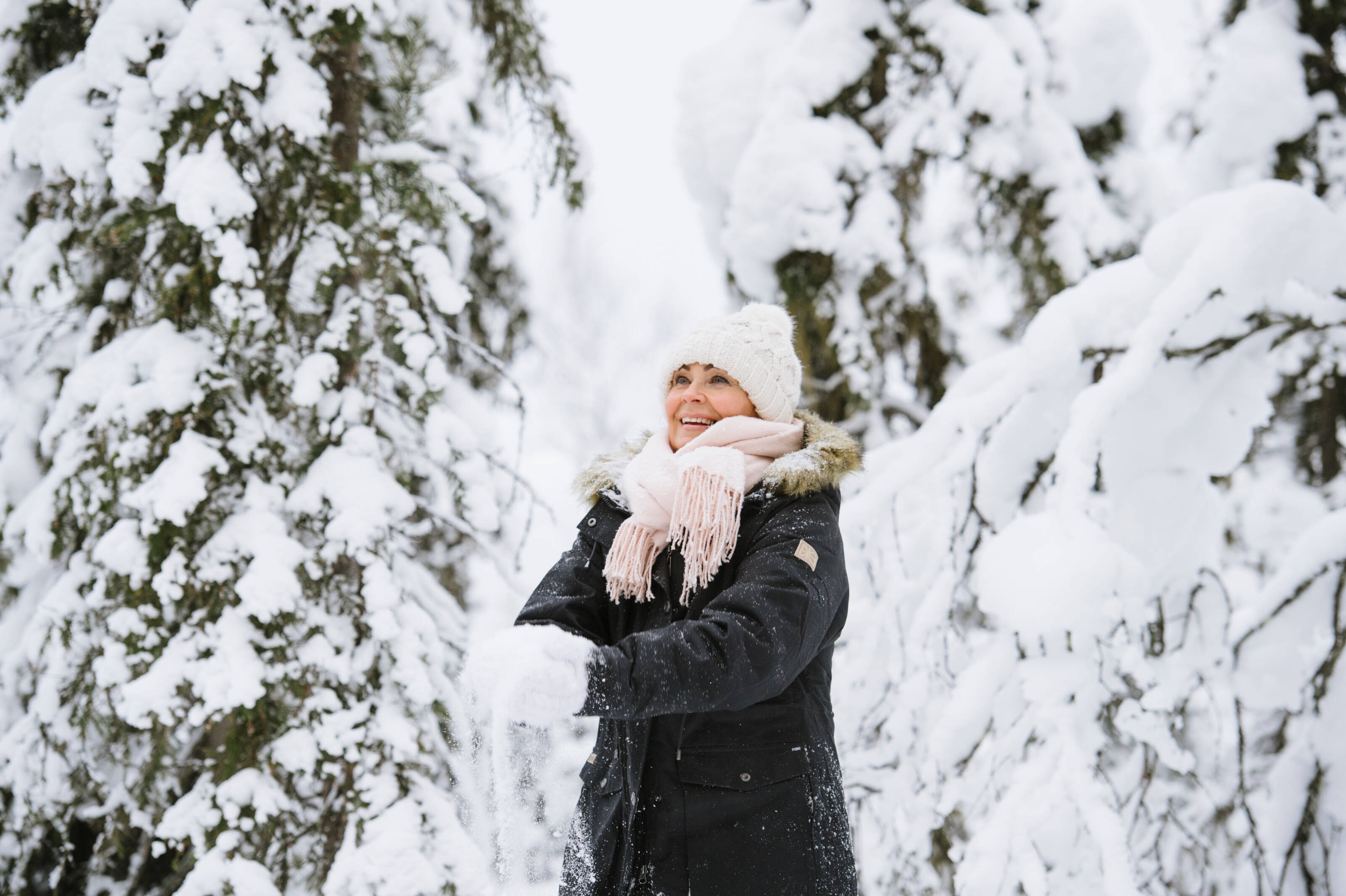 Happy woman in the midst of snowy pine trees in Finland.