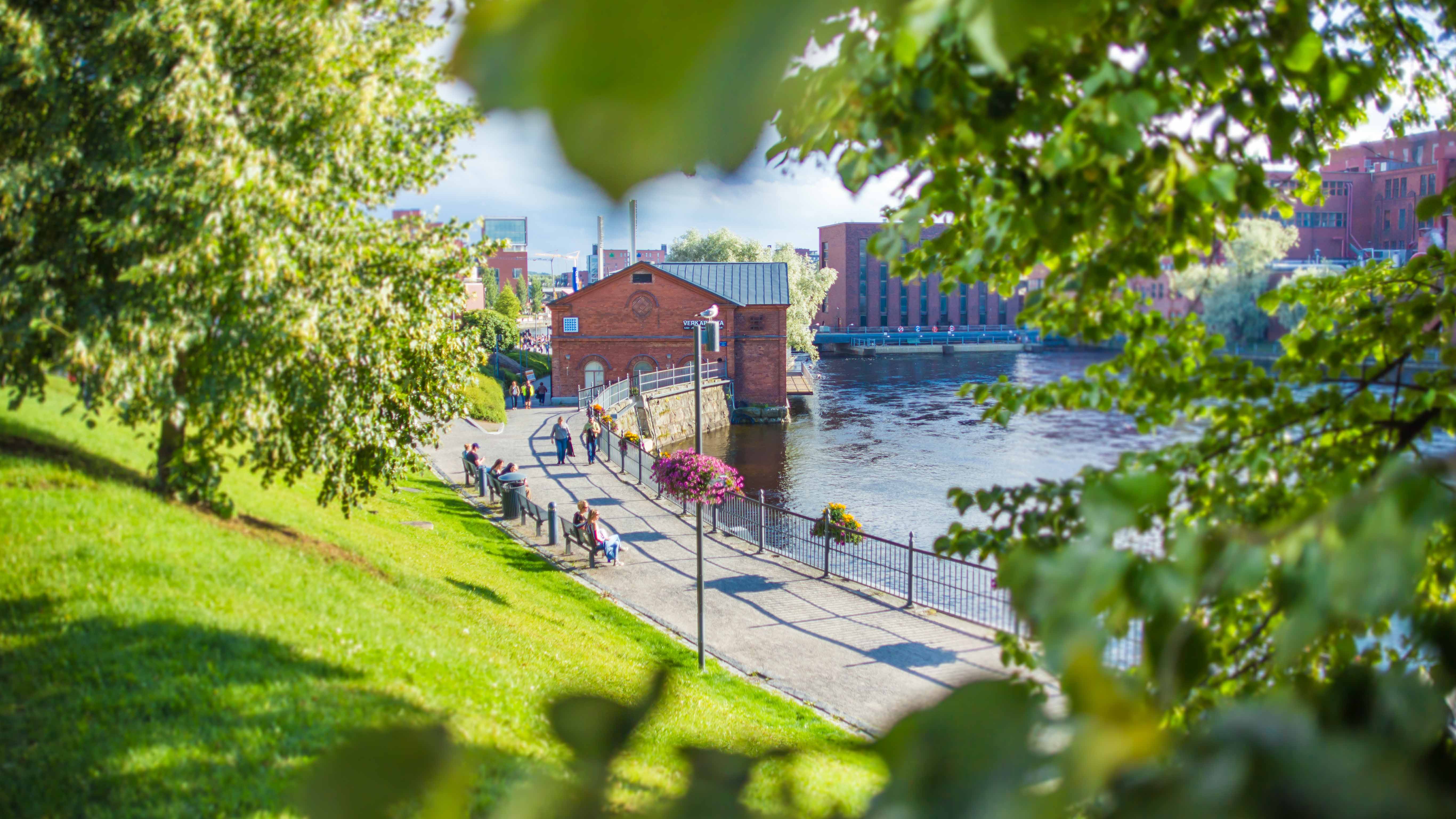 A sunny park on the shore of the Tammerkoski rapid full of people in Tampere.