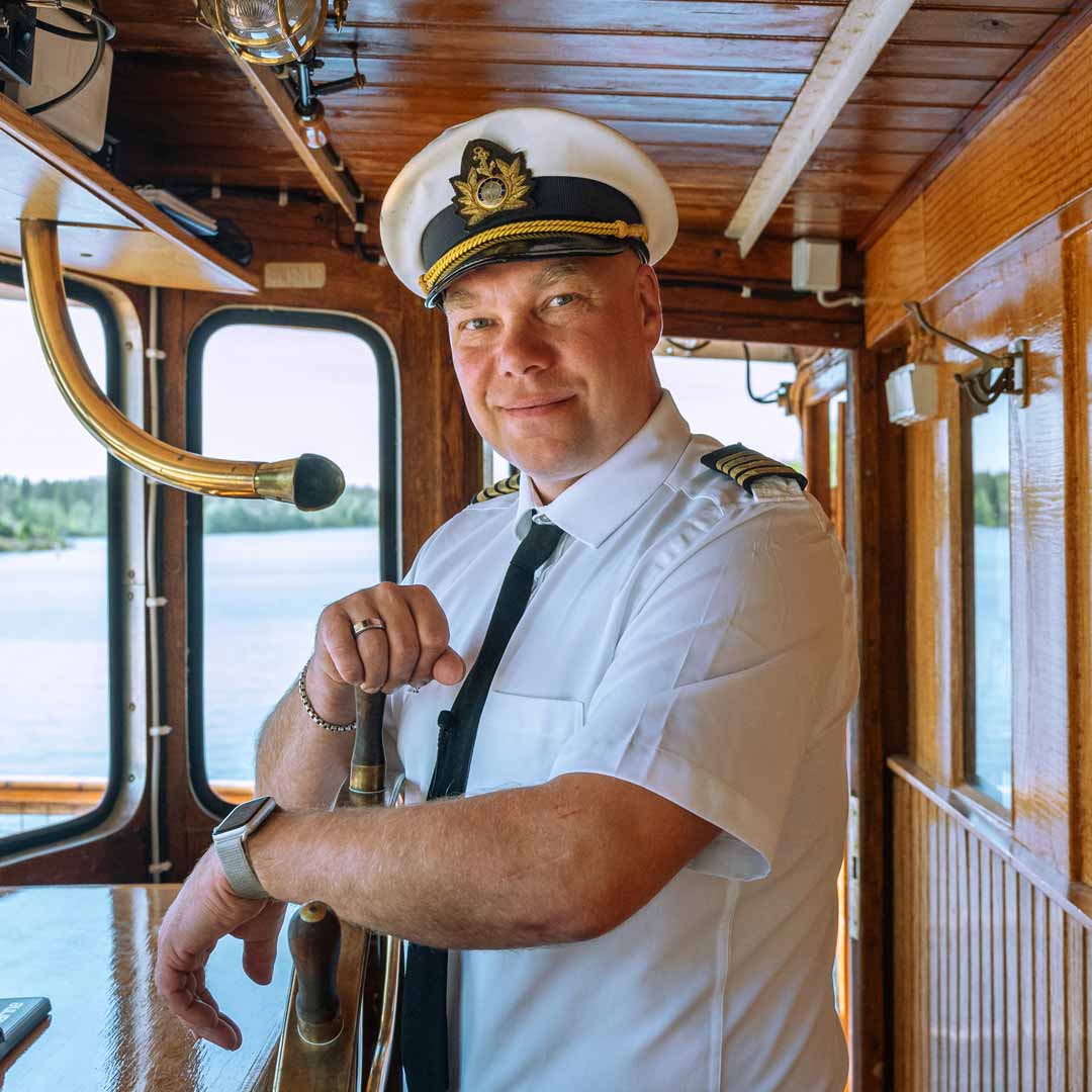 The captain of a steamboat standing on a deck while smiling at the camera in Finnish Lakeland.