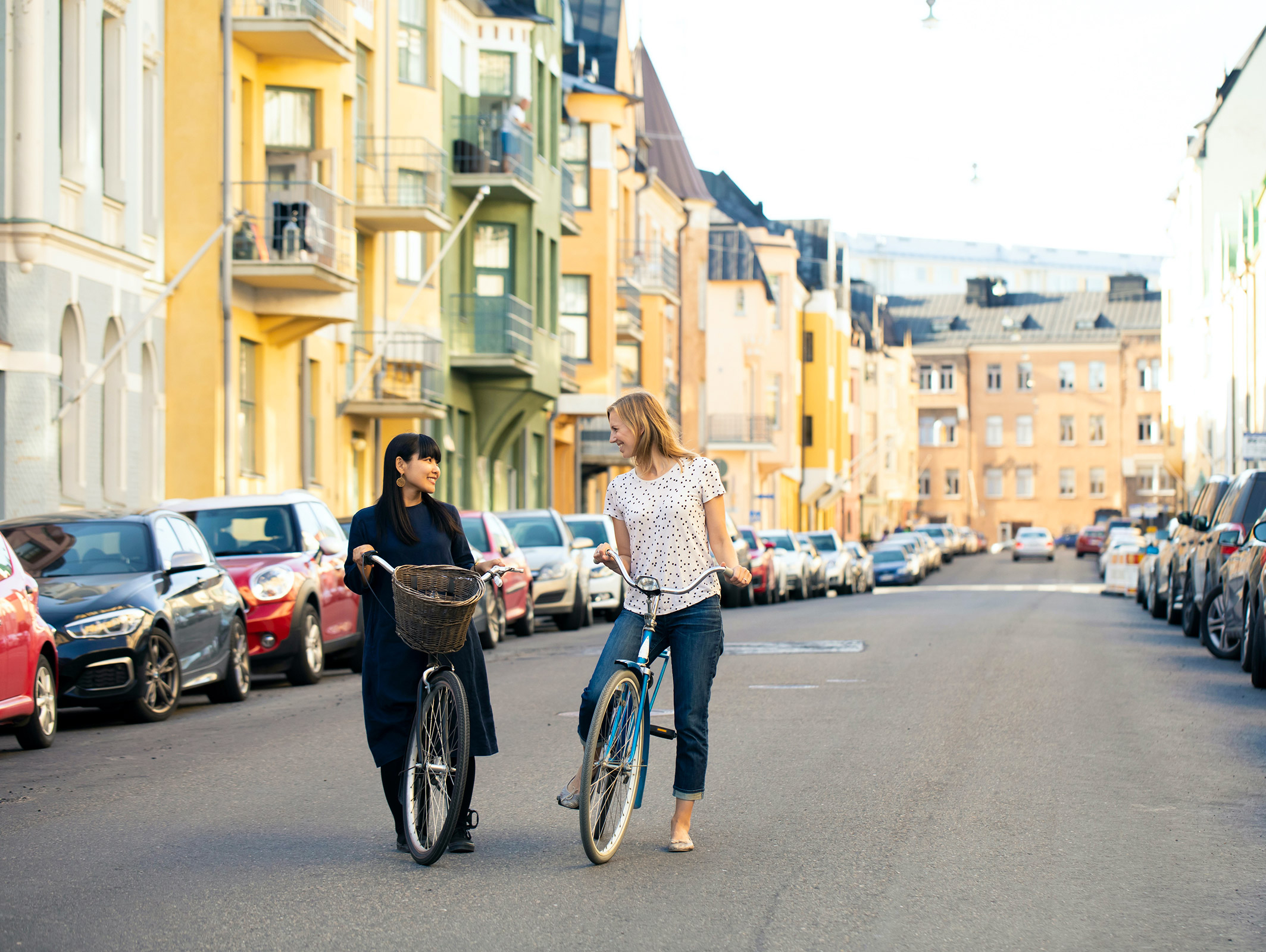 Two people smiling and talking on bikes in the middle of the street in Helsinki Finland