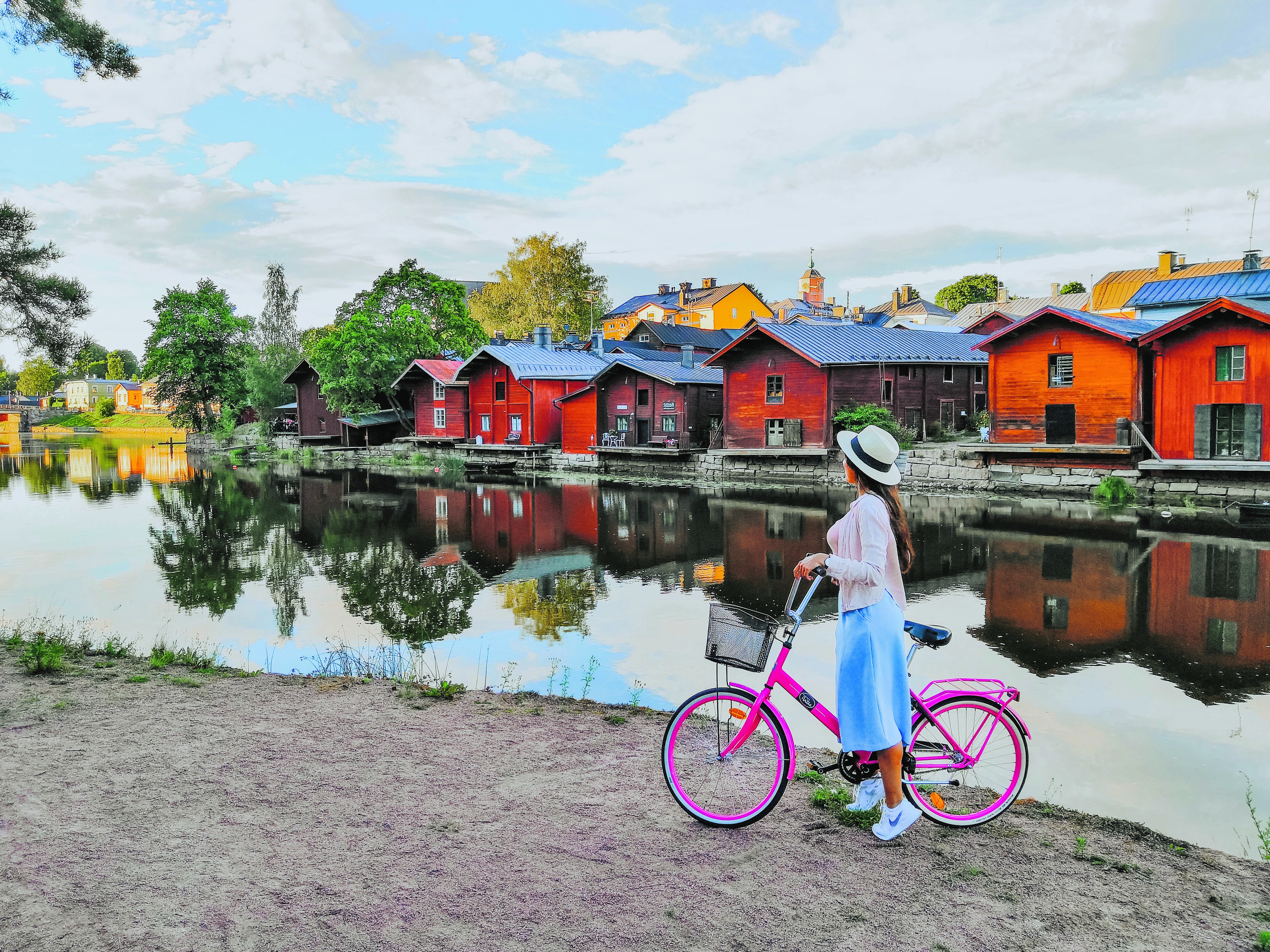 a woman looking over a river at old red ochre painted wooden buildings